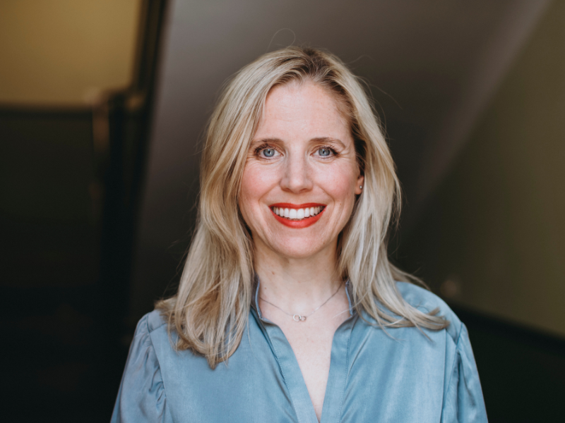 Porträt von Dr. Sarah Müller, lächelnd, mit blonden Haaren und blauer Bluse, vor unscharfem Hintergrund.